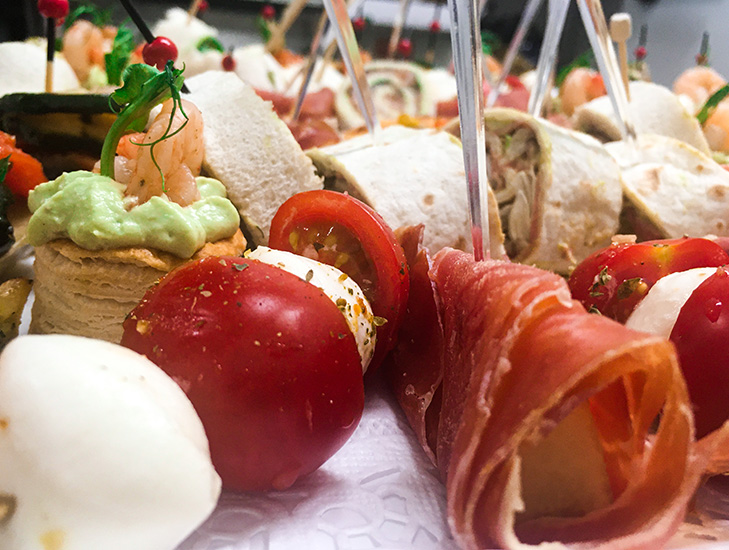 Verschiedene Häppchen mit Tomaten, Mozzarella, Schinken, Garnelen und Wraps auf einem Tablett